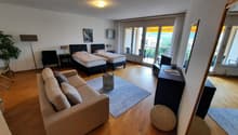 Two twin beds, couch, side tables, TV, lamps, rug, large windows, balcony with chairs