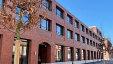 Red brick building, glass windows, modern design, multiple doors, empty parking lot, a tree in front