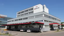 A multi-story commercial building with the Technomag logo prominently displayed. The building has large windows and a parking area in front.