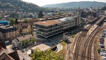 Building with multiple stories, green roof, glass windows, parking lot, train tracks