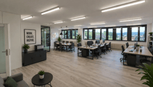 modern office space with wooden floors, large windows, desks, chairs, plants, motivational quote on wall
