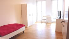 white single bed, white wooden flooring, white cabinets, desk, TV stand, television, large windows, balcony