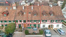 2-story building with red tiled roof, red and white color scheme, green shutters, and a small courtyard in the front