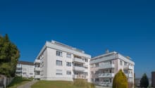 Modern apartment building, white exterior, multiple balconies, landscaped garden, driveway