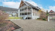 modern house, 3 stories, large balcony, metal railings, grey gravel driveway, mountain in background