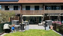 2 story house, brown roof, solar panels, wooden balcony, outdoor seating area, garden, patio