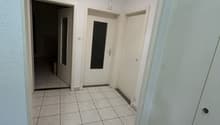 Empty hallway with white tiles, white walls, and white doors. A ceiling light is on.