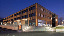 modern multi-story building, brown exterior, glass windows, ground-level storefront, stairs, parking sign