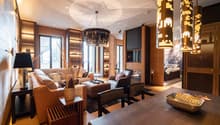 Fireplace, chandelier, couch, armchairs, side table, coffee table, rug, lamps, wooden floor, wood-paneled walls