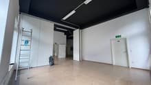 Empty room, black ceiling, white walls, tiled floor, open doors, metal ladder, trash bin