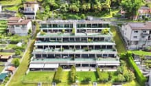 Multi-story apartment building with balconies, surrounded by lush greenery and trees