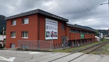 A multi-story red brick building with a flat roof, located next to a train track. The building appears to be a commercial or industrial facility.