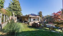 modern-style house, yellow walls, 3-story, large windows, outdoor seating, lawn, trees, mountains in background