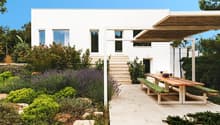 Modern white house, large windows, wooden pergola, outdoor dining area, garden with various plants