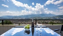 Table with view of mountains and city, bottle of champagne and two wine glasses