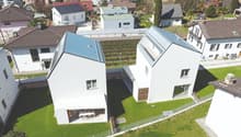 Modern white houses with solar panels on the roof, surrounded by a green lawn and a fence, aerial view