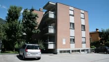 Multistory building, red bricks, several windows, balconies, parking in front