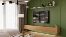 Modern living room with green accent wall, large TV display, wooden media console, pendant lighting, and a coffee table with books and decor