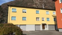 3 story yellow house, three garages in front, parking lot, mountain in the background
