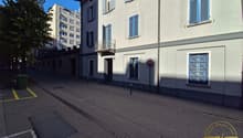 Building with multiple windows, balcony, grey walls, streetlight, trash bin, and a sign