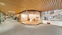 Open corridor with carpeted floor, glass walls, stairs, and a sign about renting and selling properties.
