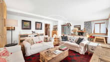 Living room with sofa, coffee table, lamps, bookshelves, decorative pillow, carpet, wooden storage box, decorative objects, stone fireplace, white curtains, paintings