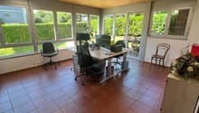 Spacious office with large windows, wooden ceiling, tiled flooring, office desk and chairs, and a cozy seating area.