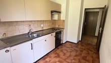 Modern kitchen with white cabinets, tiled countertops, stainless steel sink, and appliances. Brown tiled flooring.