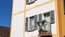 multistory building, white and yellow, four floors, balcony with plants, two windows on each floor