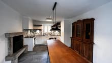 Spacious kitchen with a mix of modern and traditional elements. The kitchen features a large wooden dining table, a built-in fireplace, and a custom tile backsplash. The room also includes a wooden cabinet unit and stainless steel appliances.
