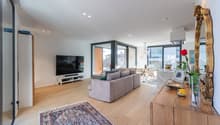 L-shaped gray sofa, large television, wooden floor, large windows, balcony, large mirror, wooden console table, flower vase, rug