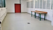 Wide empty room with white walls, white floor, red door, a wooden table, white pipes
