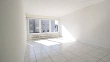 Empty room with white walls, white tiled floor, large window, white radiator