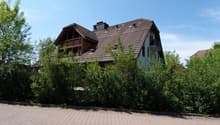 2 story house, brown roof, wooden balcony, brick wall, surrounded by bushes