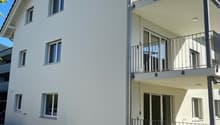 3-story apartment building with white exterior, black roof tiles, and balconies on the upper floors.