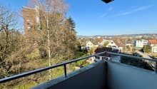 balcony with metal railing, overlooking a grassy area with trees and a building