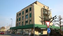 5 story building, brown walls, green roof, shops on ground floor, windows with shutters