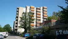 Large apartment building with balconies, orange awnings, surrounded by cars parked in designated parking spots.
