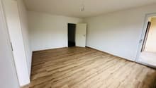 Empty room with wooden floor, white walls, two doors, one leading to another room, and a glass door leading to a balcony.
