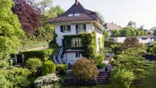 2 story house, white exterior, brown roof, balcony, surrounded by greenery