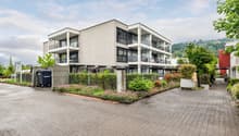 Modern apartment building with balconies, brick walls, paved driveway, greenery