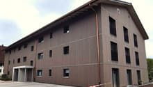 3 story building, brown exterior, multiple windows, parking area