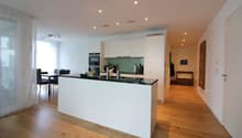 modern kitchen with white cabinets, black countertops, island, dining area, wooden floor