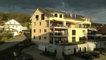 Yellow apartment building with solar panels, multiple balconies, garages and cars parked in front