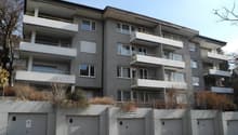multi-story apartment building with balconies, grey exterior, multiple garages