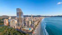 High-rise building with glass facade, swimming pool on the rooftop, surrounded by other buildings, beach, and ocean