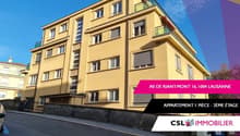 A multi-story yellow apartment building with balconies, located in Lausanne, featuring several windows, a driveway, and a bicycle parked in front.