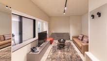 modern living room with beige walls, large windows, beige couch, TV, coffee table, rug, telephone