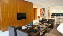 Living room with modern interior, wooden wall, couch, chair, coffee table, tv, artwork, kitchen and dining area visible in background