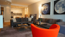 modern living room, with gray sofa, orange chair, glass tables, and flower vases